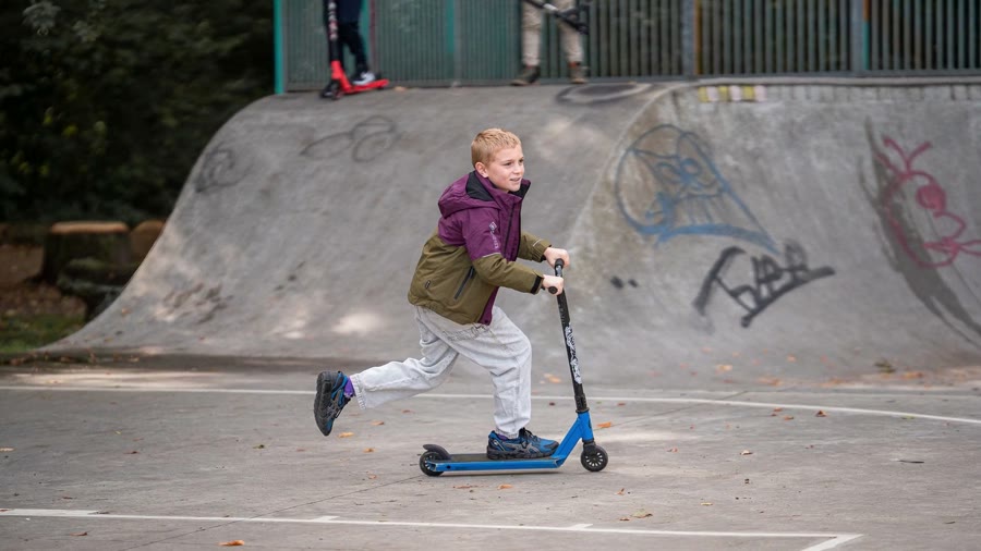 A kid in a Gore-Tex jacket on a scooter in a skate park